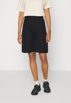 Zwarte cargoshorts met zijzakken, knielang, gemaakt van lichte stof. Gecombineerd met een beige t-shirt en zwarte sneakers.