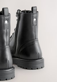 Zwarte leren enkellaarzen met een zijrits, een gestructureerde zool en aantreklusjes, met een gladde afwerking en versterkte stiksels.