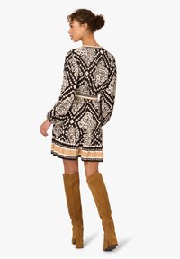 Schwarz-weiß gemustertes Kleid mit langen Ärmeln, tailliertem Schnitt und beigefarbenem Saum. Kombiniert mit kniehohen hellbraunen Stiefeln.