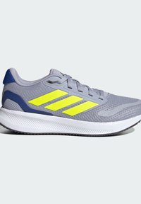 Zapatilla deportiva gris con parte superior de malla, diseño de tres rayas en amarillo neón, acentos azules, suela blanca acolchada y superficie de contacto texturizada.
