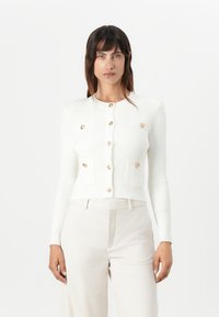 White ribbed cardigan featuring gold buttons and two front pockets, with a slightly cropped fit and long sleeves.