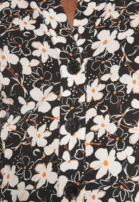 Černý oděv s květinovým vzorem bílorůžových a oranžových květin. Má zapínání na knoflíky a viditelné černé knoflíky po celé přední části.