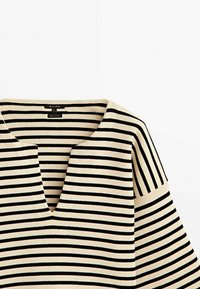 Pull en maille à rayures horizontales beige et noire avec un col en V large et une texture côtelée.