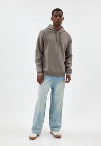 Grijze hoodie met lange mouwen, gecombineerd met lichtblauwe verwasen jeans. Beige sneakers met witte accenten maken de outfit compleet.