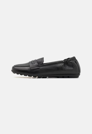 Chaussure penny loafer en cuir noir avec embout arrondi, détails cousus, dos élastiqué et semelle en caoutchouc texturée sur fond blanc.