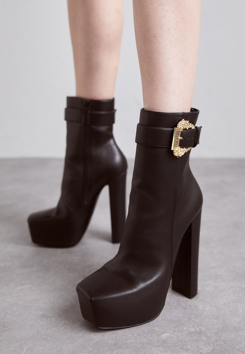 Stivali neri in pelle fino alla caviglia con punta quadrata, tacco a blocco alto e dettagli con fibbia. Caratterizzati da una superficie liscia e un design elegante.