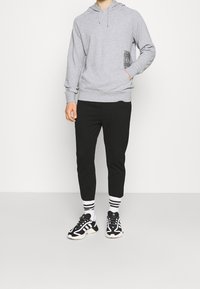 Grå hoodie med dragsko, svart fickdetalj, tillsammans med svarta tapered byxor och svarta sneakers med vita accenter och randiga strumpor.