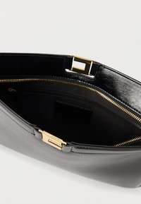 Μαύρο δερμάτινο τσαντάκι χειρός με χρυσό ορθογώνιο κούμπωμα, με μαύρο υφασμάτινο εσωτερικό και εσωτερική τσέπη με φερμουάρ.