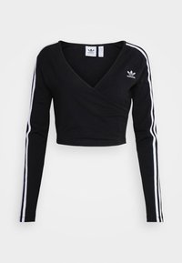 Crop top noir à manches longues avec décolleté en V, fabriqué en tissu doux, comportant deux bandes blanches le long des bras et un logo brodé sur la poitrine.