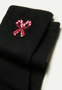 Schwarze Socken mit rot-weißer gestreifter Zuckerstangen-Stickerei, mit glatter Textur und geripptem Rand. Ordentlich gefaltet.