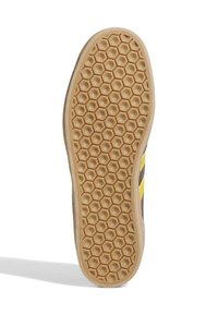 Suola di scarpa in gomma con un motivo a nido d'ape e una superficie testurizzata per la presa, di colore marrone chiaro con accenti gialli lungo i lati.