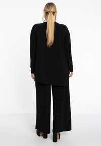 Zwarte longsleeve top met een gebogen zoom, gecombineerd met brede zwarte broek. Gladde stof, relaxte pasvorm en platform hakken.