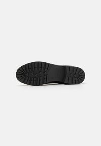 Semelle de botte en caoutchouc noir avec des crampons profonds, présentant une surface texturée et un bord lisse. Design robuste pour une meilleure adhérence et durabilité.