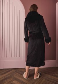 Ilgas juodas chalatas iš aksominio audinio su netikru kailio apykakle ir rankogaliais, su diržu ties liemeniu. Dėvimas su šviesios spalvos pūkuotomis šlepetėmis.