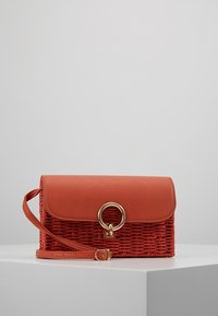 Rode geweven tas met een soepele leren klep, gouden cirkelvormige hardware en een afneembare schouderband. Kenmerkt zich door een gestructureerd ontwerp en een gestructureerde weving.