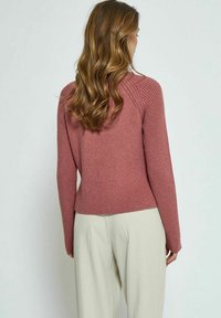 Pull mauve côtelé à manches longues et taille cintrée, associé à un pantalon beige clair. Texture lisse et détails de design subtils.