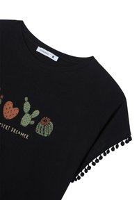 T-shirt nera a maniche corte con stampa di cactus e testo "Desert Dreamer". Presenta un bordo decorativo in pom-pom sulle maniche. Materiale in cotone.