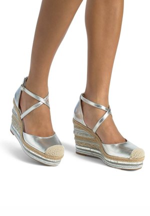 Silver metallic wedge espadrilles with crisscross ankle straps, natural jute detailing, and a rounded toe design.