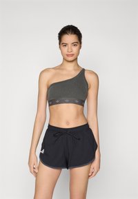 Grå sport-bh med en axel och ribbad struktur, med logoband, kombinerad med svarta shorts med dragsko, vita logodetaljer och rundad fåll.