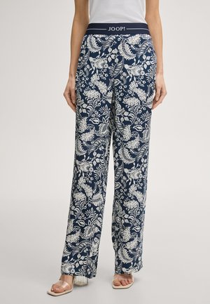 Granatowe spodnie typu wide-leg z białym kwiatowym wzorem, elastyczny pas z napisem "JOOP!", noszone z białą bluzką i sandałami na przezroczystych paskach.