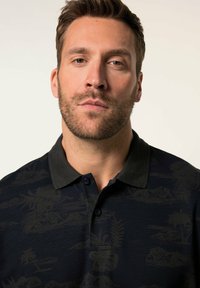 Marineblå polo t-shirt med et struktureret, tonalt mønster med palmer og bjerge. Den har en mørk krave og en to-knaps lukning.