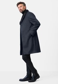 Marineblauwe wolblend overjas met een uitgesneden kraag en een slank ontwerp, gecombineerd met zwarte slim-fit broek en gepolijste Chelsea boots.