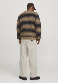 Przesadny sweter w brązowo-granatowe paski z teksturowanym wykończeniem, zestawiony z kremowymi spodniami o luźnym kroju i czarnymi butami.