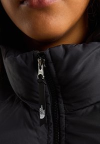 Zbliżenie na dolną część twarzy osoby ubranej w czarną kurtkę North Face z srebrnym zamkiem błyskawicznym YKK zapiętym pod szyję.