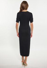 Rochie neagră, ajustată, cu mâneci lungi, textură netedă, cu tiv până la genunchi și detalii cu mânecile răsucite. Pantofi cu toc înalt, de culoare deschisă, cu bretele.