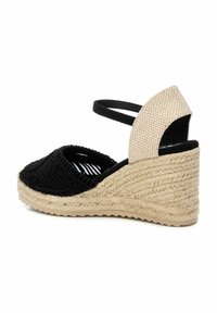Sandalia de cuña de esparto tejido en negro con un upper texturizado, correa ajustable negra y acento beige en el talón. Cuña envuelta en yute.