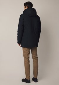 Ciemna ocieplana kurtka z kapturem, o prostym kroju. W połączeniu z khaki spodniami i czarnymi butami, na neutralnym tle.