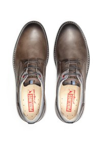Zapatos de cuero marrón con puntera redonda, diseño de cordones, detalles en gris y plantilla perforada. Nombre de la marca visible en el interior.