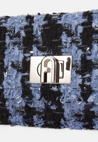 Borsa strutturata in tessuto blu e nero, con una chiusura metallica argentata decorata da un logo distintivo. Presenta dettagli lucidi.