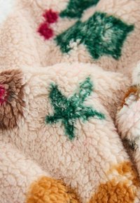 Pasztell rózsaszínű, texturált, puha anyag, amelyen zöld levelek, piros pöttyök és barna akcentusok találhatók. Meleg, bolyhos textil, ideális a kényelemért.
