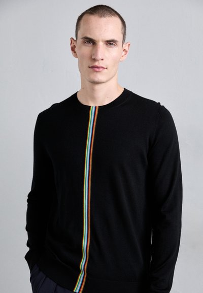 Svart strikkegenser med en vertikal regnbuestripe nedover midten. Rund hals og lange ermer med en jevn tekstur.