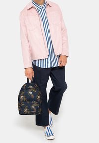 Ljusrosa mockajacka, blå och vit randig skjorta, marinblå byxor, marinblå ryggsäck med blommönster och blå och vit randiga slip-on skor.