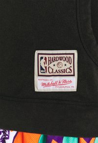 Débardeur en tissu noir présentant une étiquette rectangulaire avec l'inscription "HARDWOOD CLASSICS" et le logo NBA ; comprend des coutures et des détails texturés.