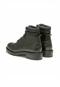 Bottines en cuir noir avec un col rembourré, un design à lacets et une semelle en caoutchouc texturé, arborant un logo "KOST" sur le côté.