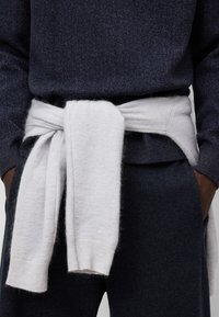 Tröja i mörkblått stickat med strukturerat mönster, knytet i midjan med ett lätt grått mjukt ullager, med ribbade mudd.