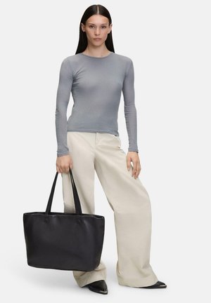 Sac en toile noir en cuir avec de longues poignées, texture lisse et design spacieux, associé à un haut à manches longues gris à côtes et un pantalon large crème.
