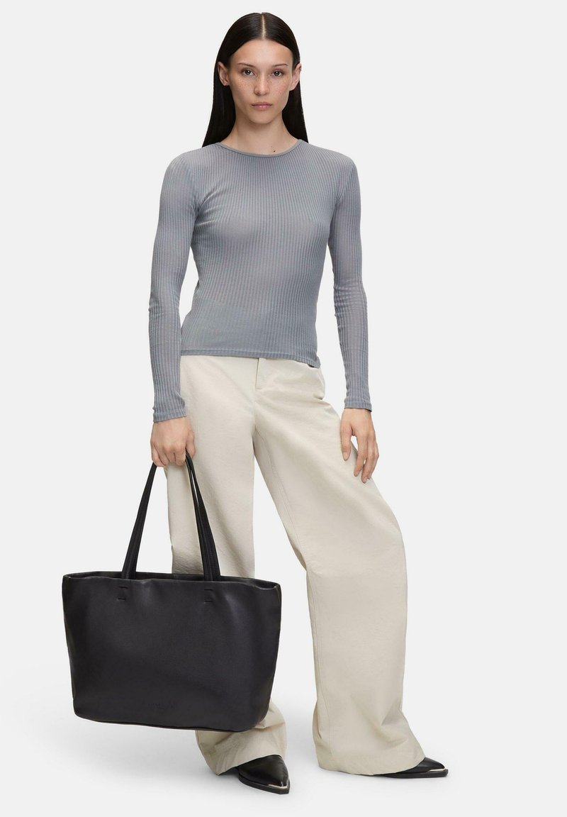 Zwarte leren totebag met lange hengsels, gladde textuur en ruim ontwerp, gecombineerd met een grijs geribbeld longsleeve-top en crèmekleurige wijde broek.