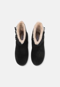 Botas de ante negras hasta el tobillo con un suave forro de piel de pelo beige, que cuentan con cordones decorativos y un botón lateral para un ajuste ajustable.