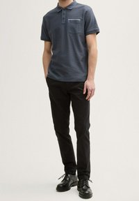 Polo bleu marine à manches courtes avec un motif texturé, doté d'une poche. Associé à un pantalon noir ajusté et des chaussures noires à lacets.