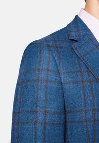 Niebieska, w kratę, wełniana marynarka z wyraźnymi ramionami i klapami z wcięciem, z brązowymi liniami podkreślającymi wzór kraty.