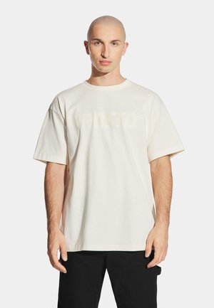 Kremowy bawełniany T-shirt z krótkim rękawem, z dużym, subtelnym nadrukiem logo. Luźny krój z okrągłym dekoltem.