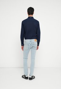 Laivastonsininen pitkähihainen paita, jossa on kauluskäänteet, yhdistetty vaaleansinisiin slim fit -farkkuihin. Farkuissa on takana tan-nahkainen merkki.