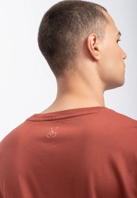 T-shirt color ruggine con collo a giro, dotata di un piccolo logo ricamato sul retro. Materiale morbido con una vestibilità comoda.