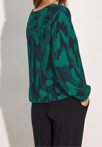 Koszula drukowana w zielonym i ciemnym turkusie, lekki materiał, luźny fason, długie rękawy z elastycznymi mankietami, okrągły dekolt, subtelna tekstura.