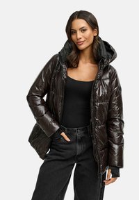 Skinnende sort pufferjakke med hætte, quiltet design, frontlynlås og elastiske manchetter, parret med en sort top og mørke jeans.