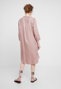 Dlouh dress s růžovou barvou a vzorovaným designem, tříčtvrteční rukávy, detail záhybu na zadní straně a boční rozparky, doplněný o ploché černé sandály.